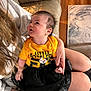adult, baby, black_skirt, casual_clothing, child, couch, cozy, curious, cute, family, holding, indoor, infant, looking_up, person, portrait, rug, sitting, wooden_floor, yellow_shirt