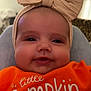Millie joined the competition — help win amazing prizes! baby, child, infant, headband, bow, orange_shirt, smile, face, cute, apparel, closeup, portrait, indoors, happy, person, young_child, sitting, clothing, text_on_clothing, headwear