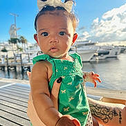 Layla is registered to the contest to win money with this photo: baby, child, infant, green_dress, bow, tattoo, hand, marina, boat, water, dock, sunlight, outdoor, sky, cloud, person, portrait, cute, expression, summer