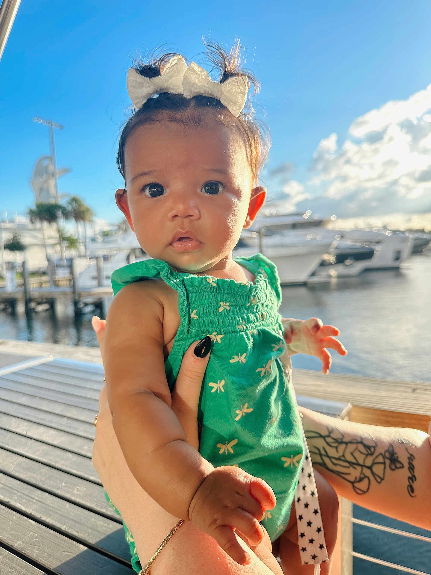 Layla is registered to the contest to win money with this photo: baby, child, infant, green_dress, bow, tattoo, hand, marina, boat, water, dock, sunlight, outdoor, sky, cloud, person, portrait, cute, expression, summer