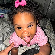 Ayla is registered to the contest to win money with this photo: toddler, child, baby, pink_bow, curly_hair, tongue_out, crawling, hand, blanket, indoor, bedroom, person, smiling, cute, playful, closeup, face, happy, clothing, infant