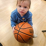 Ezra is registered to the contest to win money with this photo: toddler, child, basketball, blue_hoodie, wooden_floor, indoor, barefoot, bag, toy, floor, person, casual_clothing, young_child, curious_expression, sports_equipment, hand, foot, playing, candid, portrait