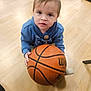 toddler, child, basketball, blue_hoodie, wooden_floor, indoor, barefoot, bag, toy, floor, person, casual_clothing, young_child, curious_expression, sports_equipment, hand, foot, playing, candid, portrait