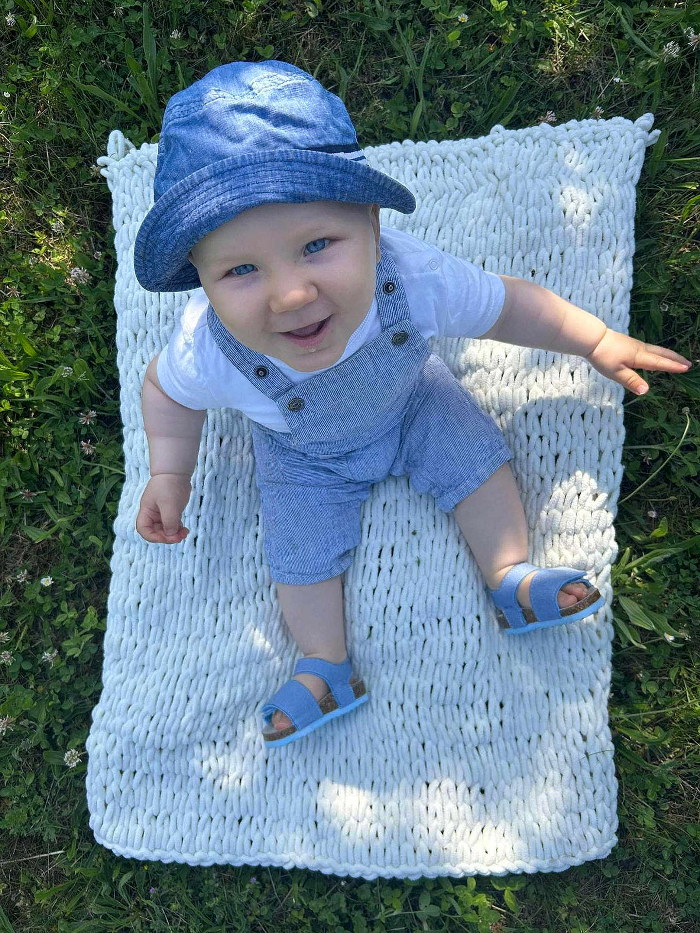 Maëlo participe au concours pour gagner de l'argent avec cette photo : baby, child, blue_hat, blue_overalls, sandals, knitted_blanket, grass, outdoor, smiling, happy, sitting, summer, sunlight, greenery, cute, portrait, infant, nature, playful, fun
