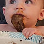 baby, child, chocolate, closeup, curious, cute, eating, expression, face, food, hand, high_chair, holding, indoor, messy, mouth, person, plate, seat, young