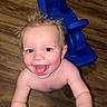 toddler, child, smiling, happy, bare_chest, blue_toy, wooden_floor, indoor, playful, face, hair, reaching, excited, young_child, person, infant, cute, baby, expression, fun