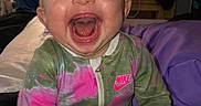 Emerson is registered to the contest to win money with this photo: baby, laughing, onesie, nike, pacifier, bed, blanket, indoor, child, happy, person, clothing, infant, smiling, hand, face, head, sitting, home, cozy