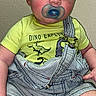 Emerson is registered to the contest to win money with this photo: baby, pacifier, dino_explorer, yellow_shirt, striped_overalls, sitting, curious, child, indoor, portrait, blond_hair, cute, infant, face, skin, clothing, feet, hands, expression, young