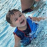 Xander is registered to the contest to win money with this photo: child, smiling, water, pool, splashing, life_vest, summer, fun, happy, outdoor, swimming, wet_hair, active, playful, boy, water_droplets, recreation, leisure, person, blue