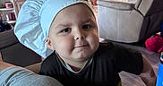 Xander is registered to the contest to win money with this photo: toddler, child, chef_hat, smiling, indoors, living_room, television, furniture, couch, recliner, person, cute, playful, young_child, home, kitchen, cabinet, floor, light, expression