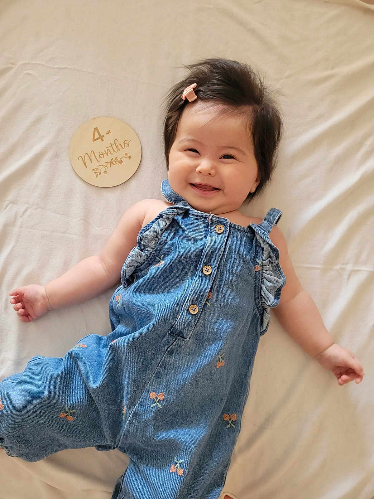 Leah joined the competition — help win amazing prizes! baby, smiling, denim, clothing, infant, hair_clip, plaque, milestone, bed, soft, cute, portrait, child, happy, lying_down, fabric, button, cherry_pattern, skin, indoor