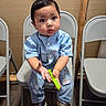 toddler, child, boy, blue_shirt, ripped_jeans, sneakers, folding_chair, indoor, toy, curious, seated, wood_floor, casual_clothing, short_hair, expression, furniture, background_wall, hand_gesture, young_child, playful