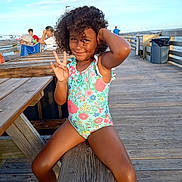Amazin Miller is registered to the contest to win money with this photo: child, girl, curly_hair, swimsuit, peace_sign, pier, wooden_deck, sunlight, ocean, fishing, people, outdoor, summer, smile, playful, vacation, nature, relaxation, casual, daytime