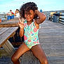 child, girl, curly_hair, swimsuit, peace_sign, pier, wooden_deck, sunlight, ocean, fishing, people, outdoor, summer, smile, playful, vacation, nature, relaxation, casual, daytime
