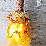 child, girl, princess_costume, yellow_dress, glowing_dress, tiara, smiling, portrait, indoor, stone_wall, lighting, gloves, bow, fashion, happy, cute, young, costume, fairy_tale, dress_up