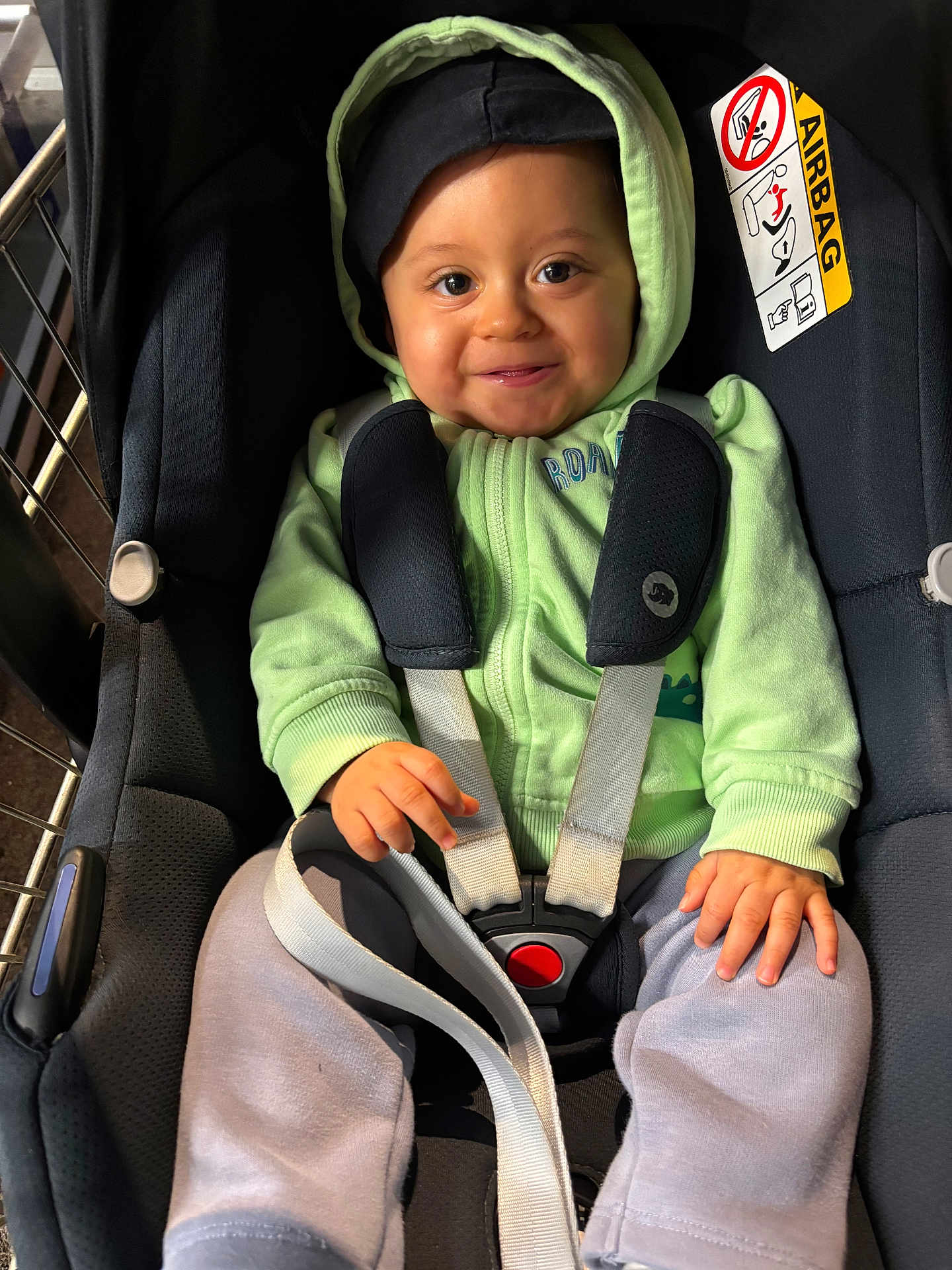 Noé participe au concours pour gagner de l'argent avec cette photo : baby, child, car_seat, harness, green_hoodie, gray_pants, smiling, happy, face, hand, safety, seatbelt, infant, cute, indoors, person, clothing, portrait, closeup, seat