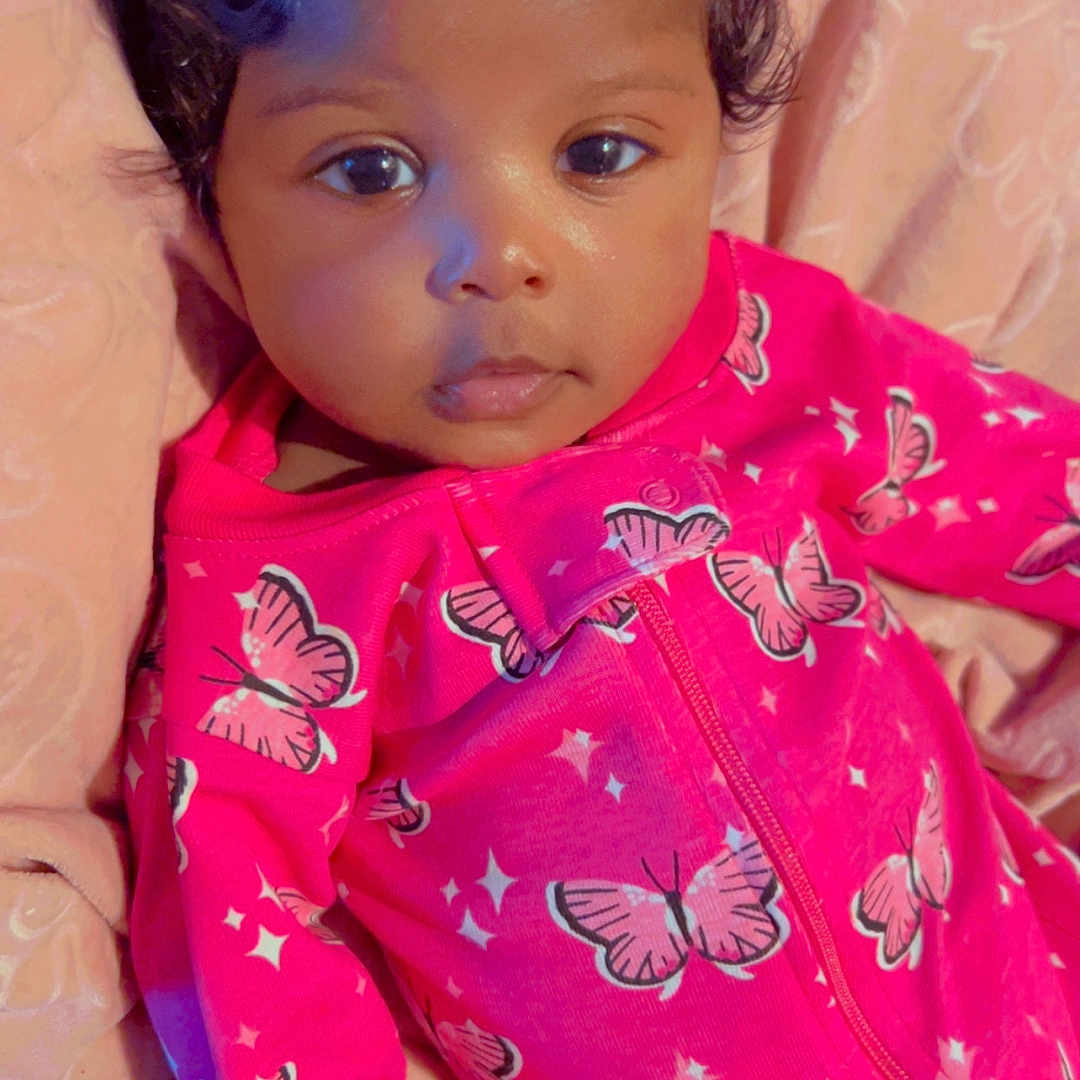 Aylah is registered to the contest to win money with this photo: baby, blanket, butterfly_pattern, child, comfort, cuddly, curly_hair, cute, eyes, face, hand, holding_finger, indoor, infant, newborn, person, pink_outfit, portrait, sleepwear, soft_texture