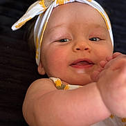 Angel is registered to the contest to win money with this photo: baby, child, headband, yellow, white, flower_pattern, smiling, face, arm, skin, closeup, portrait, infant, happy, cute, lying_down, background, soft_light, clothing, baby_girl