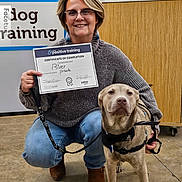River is registered to the contest to win money with this photo: achievement, award, casual_clothing, certificate, certificate_of_completion, concrete_floor, dog, glasses, happy, harness, indoor, kneeling, leash, petco, positive_training, short_hair, smiling, training, woman, wooden_cabinet