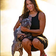 Smokey is registered to the contest to win money with this photo: woman, dog, french_bulldog, pet, outdoor, sunlight, golden_hour, black_clothing, squatting, affection, animal, canine, young_adult, casual, footwear, pink_slippers, tattoo, bracelet, leash, nature