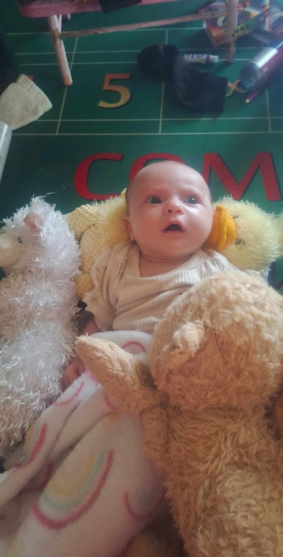Imani joined the competition — help win amazing prizes! baby, infant, stuffed_animal, blanket, plush_toy, soft_toy, child, floor_mat, number_five, colorful, gazing, indoors, cute, young_child, cozy, comfort, play_area, toy, expression, person