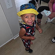 Ryland joined the competition — help win amazing prizes! toddler, child, smiling, hat, bucket_hat, colorful_clothing, indoor, wooden_floor, dog, black_and_white_dog, person, sneakers, happy, playful, floor, wall_outlet, adult, seated, flooring, home