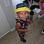 toddler, child, smiling, hat, bucket_hat, colorful_clothing, indoor, wooden_floor, dog, black_and_white_dog, person, sneakers, happy, playful, floor, wall_outlet, adult, seated, flooring, home