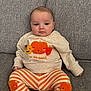 baby, infant, child, sitting, couch, gray_couch, sweater, pumpkin_design, striped_pants, orange_stripes, clothing, cute, indoors, portrait, face, person, comfort, cozy, young_child, expression