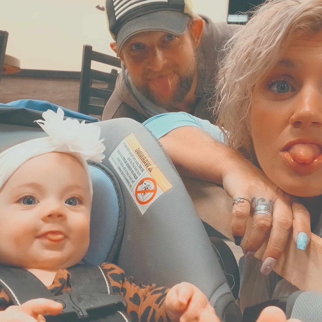 Emma J is registered to the contest to win money with this photo: baby, car_seat, child, expression, family, fun, hat, headband, humor, indoor, jacket, man, nail_polish, people, playful, portrait, rings, smile, tongue_out, woman