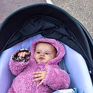Selena participe au concours pour gagner de l'argent avec cette photo : baby, child, stroller, pink_jacket, hood, blanket, outdoor, curious, infant, clothing, cold_weather, cute, young, person, portrait, hand, face, cozy, baby_clothes, baby_accessory