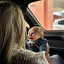 Asher is registered to the contest to win money with this photo: baby, smiling, adult, inside_car, blue_clothing, person, holding, joy, happy, infant, head, face, hair, seat, window, car_interior, seatbelt_warning, light, blurred_background, casual