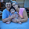 baby, child, elderly_woman, glasses, outdoor, table, holding, family, casual_clothing, portrait, skin, arm, face, person, sitting, love, affection, relaxed, multigenerational, expression