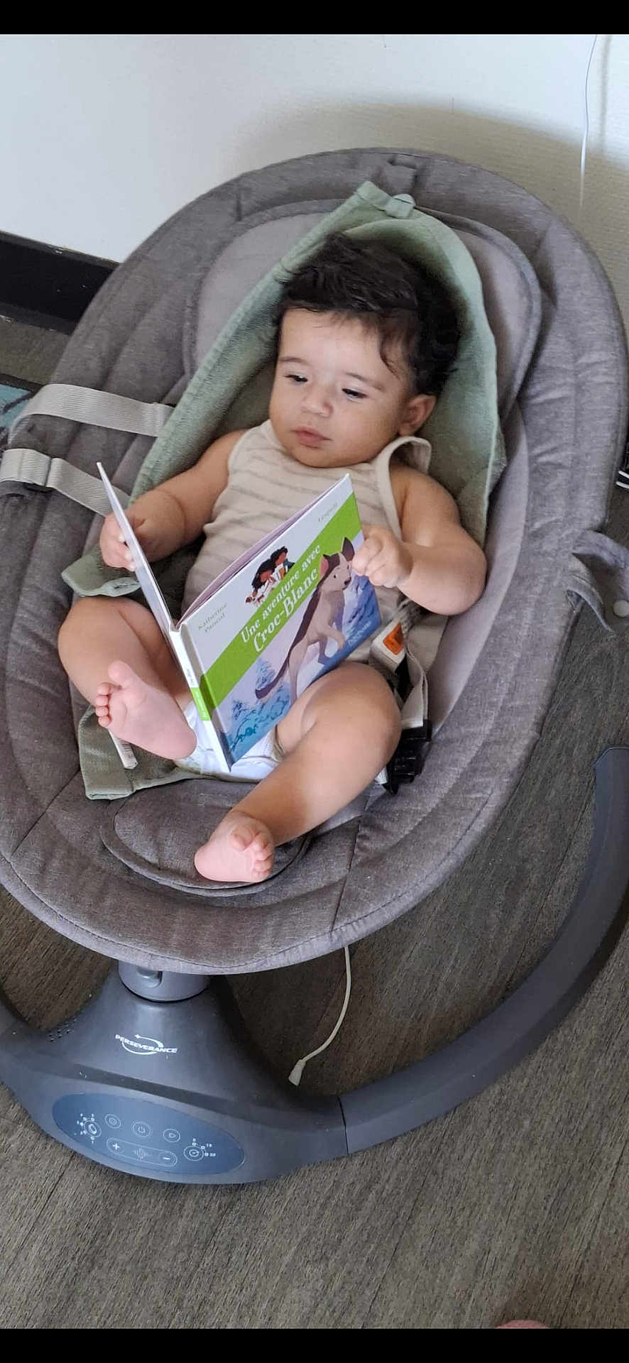 Daniel participe au concours pour gagner de l'argent avec cette photo : baby, child, book, reading, baby_rocker, seat, indoor, floor, foot, hand, curly_hair, clothing, modern, technology, device, relaxing, expression, person, infant, engaged