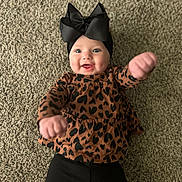 Ivory is registered to the contest to win money with this photo: baby, infant, child, black_bow, headwear, brown_top, heart_pattern, black_pants, carpet, smiling, happy, reaching_hands, indoors, cute, portrait, person, young_child, playful, fashion, closeup