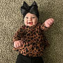 baby, infant, child, black_bow, headwear, brown_top, heart_pattern, black_pants, carpet, smiling, happy, reaching_hands, indoors, cute, portrait, person, young_child, playful, fashion, closeup