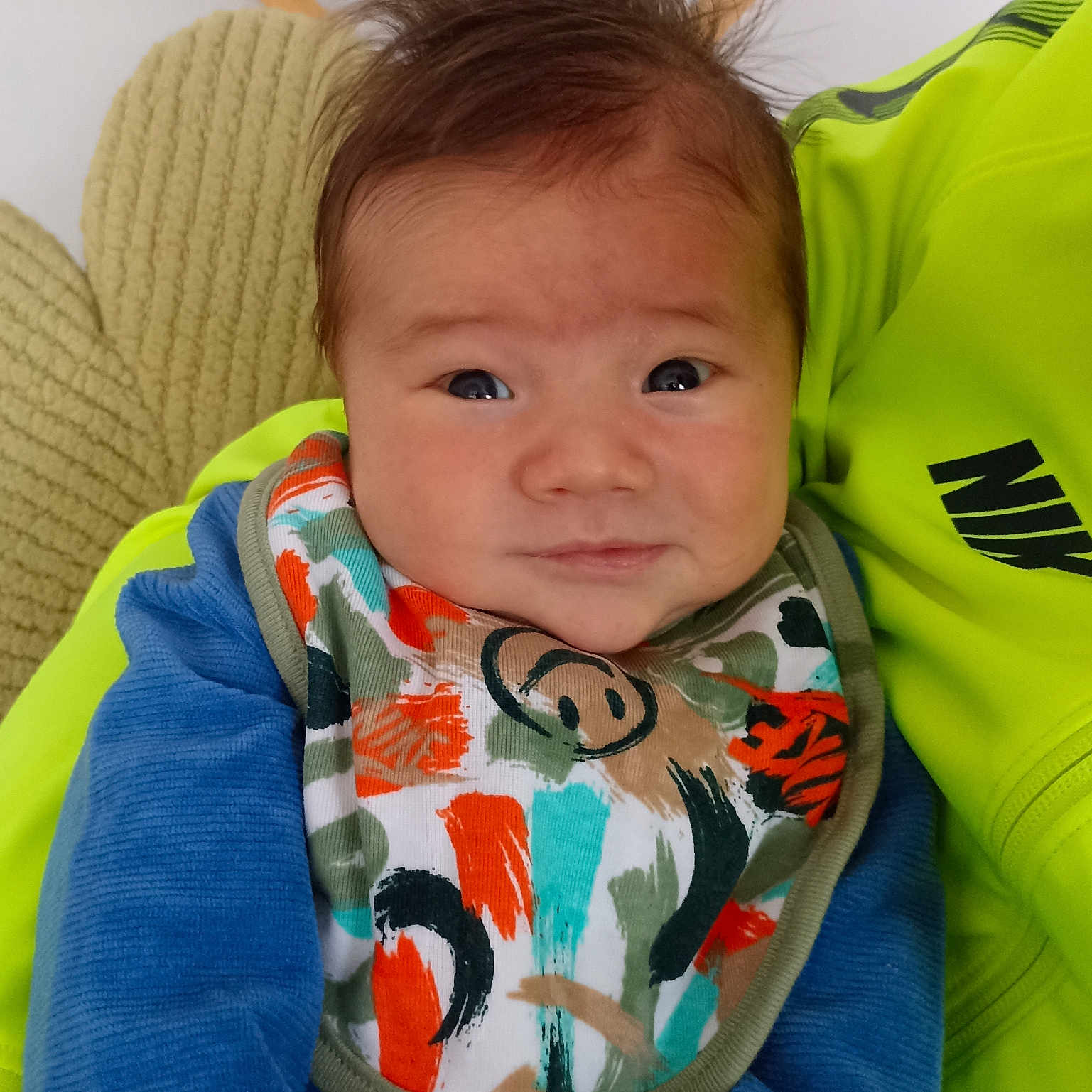 Tao a rejoint le concours — aidez-le/la à gagner de superbes lots ! baby, bib, blue_clothing, closeup, colorful, cushion, cute, expression, fabric, face, hair, indoor, infant, neon_green, person, portrait, sitting, smile, soft_texture, young_child