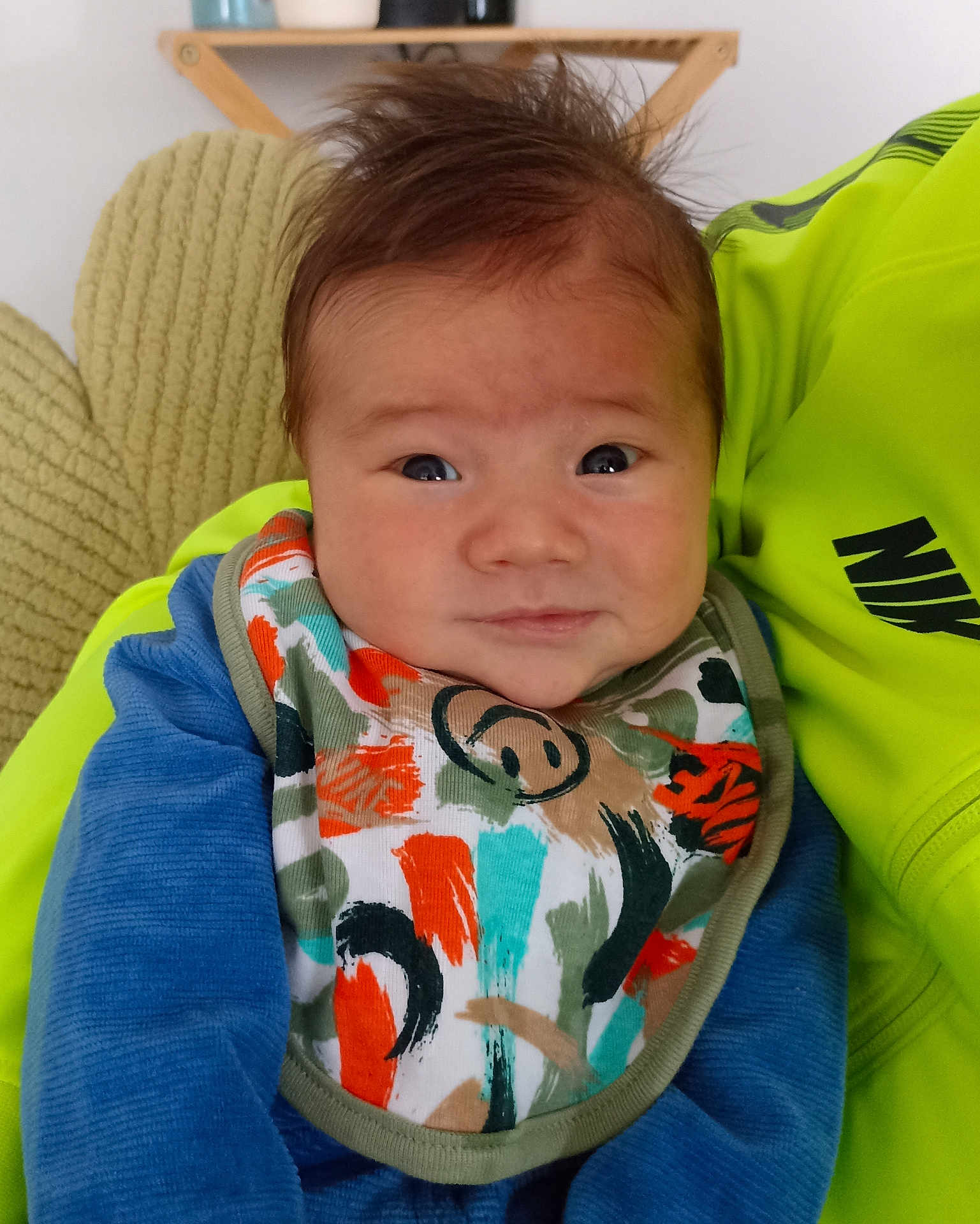 Tao a rejoint le concours — aidez-le/la à gagner de superbes lots ! baby, infant, face, bib, blue_clothing, hair, expression, person, portrait, closeup, indoor, cushion, fabric, colorful, neon_green, smile, young_child, cute, soft_texture, sitting