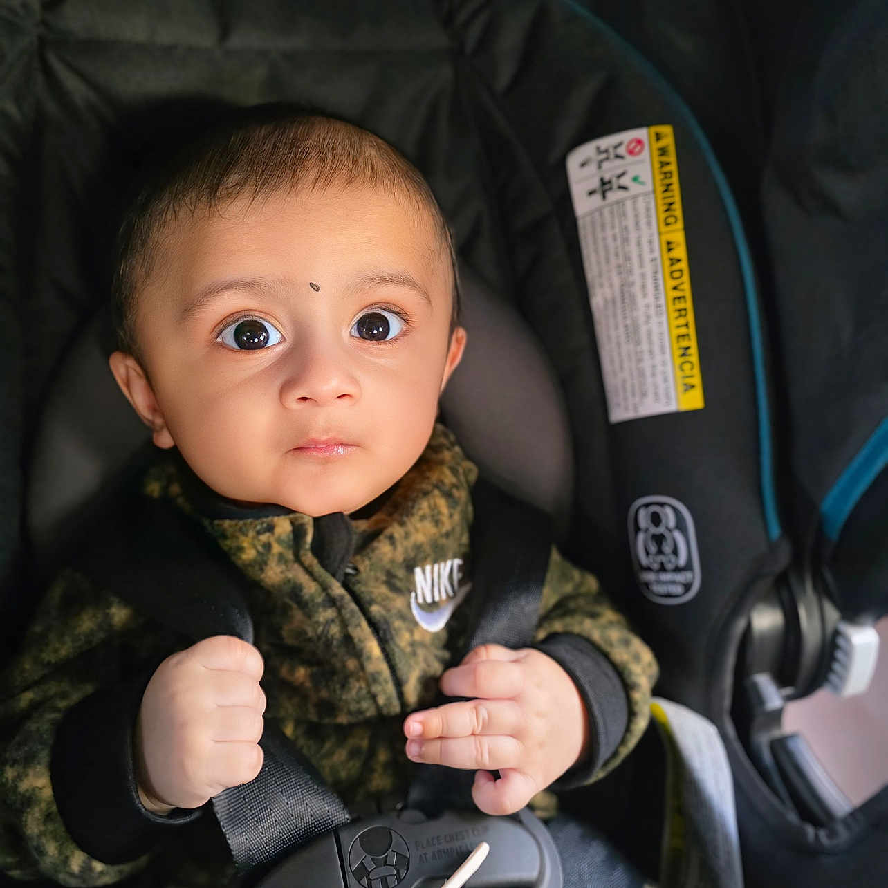 Atharv joined the competition — help win amazing prizes! baby, camo, car_seat, child, clothing, cute, expression, face, hands, indoors, infant, jacket, nike, portrait, safety_harness, seatbelt, secure, straps, wide_eyes, young_child