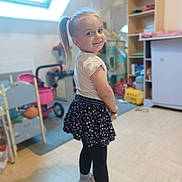 Diana participe au concours pour gagner de l'argent avec cette photo : casual_clothing, child, cute, floor, furniture, girl, happy, indoor, leggings, natural_light, person, playroom, pony_tail, shelf, skirt, smiling, socks, toys, window, young
