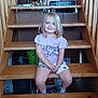 child, girl, stairs, wooden_stairs, smile, blonde_hair, casual_clothing, indoor, home, wood, sitting, happy, young, tshirt, shorts, person, furniture, relaxed, portrait, cute