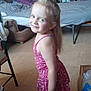 child, girl, smiling, pink_dress, barefoot, indoor, bed, fan, chair, floor, laundry_rack, clothes, bag, wooden_floor, furniture, portrait, happy, standing, blonde_hair, home