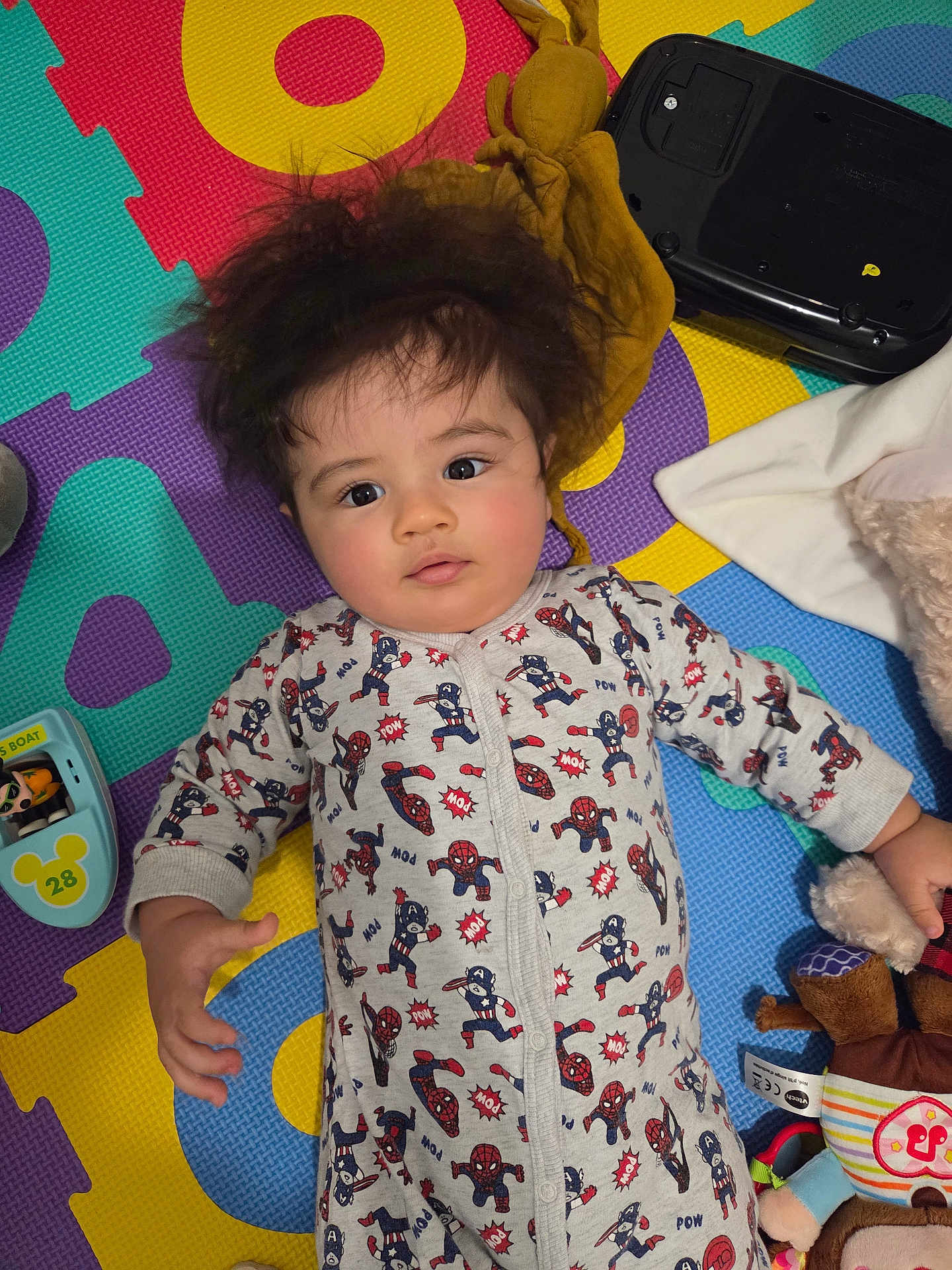 Giulio participe au concours pour gagner de l'argent avec cette photo : baby, child, infant, onesie, superhero, puzzle_mat, toy, plush_toy, colorful, indoor, floor, curly_hair, cute, lying_down, playtime, face, expression, young_child, casual, home