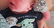 Bennett is registered to the contest to win money with this photo: baby, carpet, clothing, couch, cute, face, footwear, gaze, hand, head, holding, indoors, infant, legs, mittens, newborn, onesie, person, skin, tattoo