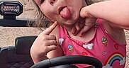 Rosalia is registered to the contest to win money with this photo: child, girl, playful, silly_face, pink_clothing, rainbow, ice_cream_cone, toy_car, steering_wheel, outdoor, dirt_road, vehicle, curly_hair, red_bow, expression, fun, portrait, person, casual, daylight