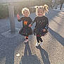 child, children, girl, halloween, face_paint, holding_hands, outdoor, daylight, shadow, pavement, costume, skirt, sneakers, smile, person, cute, playful, sunlight, friends, happy