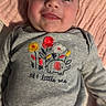 Brooklyn is registered to the contest to win money with this photo: baby, smiling, infant, blanket, clothing, red_pants, grey_shirt, embroidery, elephant, flowers, face, person, child, cute, happy, laying_down, indoors, soft_texture, portrait, closeup