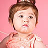 Noelle is registered to the contest to win money with this photo: child, toddler, girl, portrait, close_up, face, smiling, pink_background, peach_dress, hair_bow, brown_hair, brown_eyes, baby, sitting, indoors, studio, milk_mustache, hand, rosy_cheeks, photography