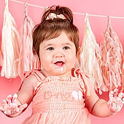 Noelle is registered to the contest to win money with this photo: baby, child, infant, portrait, smiling, happy, pink, dress, bow, hair, hands, frosting, cake_smash, birthday, party, backdrop, tassels, indoor, sitting, closeup