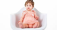 Noelle is registered to the contest to win money with this photo: baby, child, toddler, portrait, sitting, chair, white_background, pink_dress, dress, hair_bun, topknot, facial_expression, serious, pouting, barefoot, indoor, studio, furniture, fashion, photography