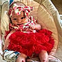 baby, infant, headband, bow, red_skirt, strawberry_pattern, clothing, baby_seat, blanket, cushion, foot, hand, cute, indoors, comfort, portrait, child, person, soft_toy, fabric